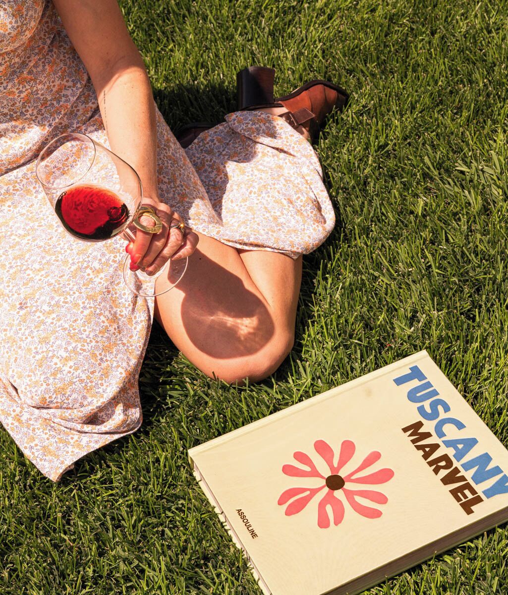 Una persona recostada sobre el césped con un libro titulado "Tuscany Marvel" a su lado.