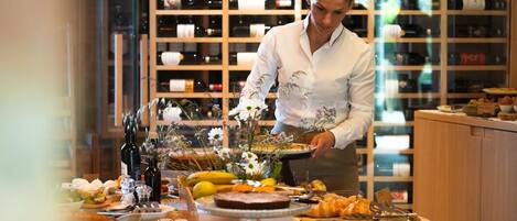 A person serving food at a buffet with a wine cellar in the background.