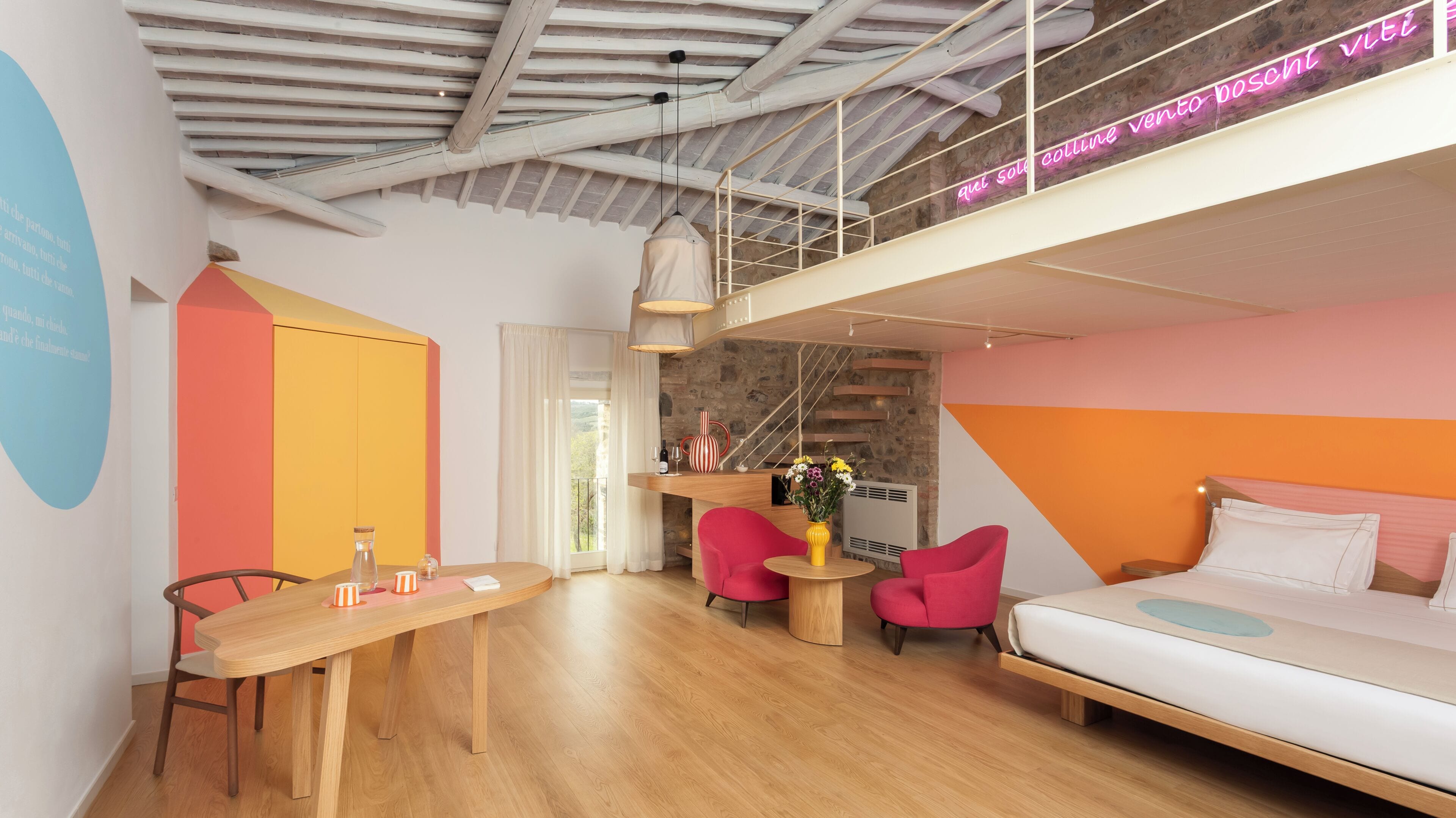 A modern hotel room with a loft bed, a dining table with chairs, a small kitchen area, and a balcony with a neon sign.