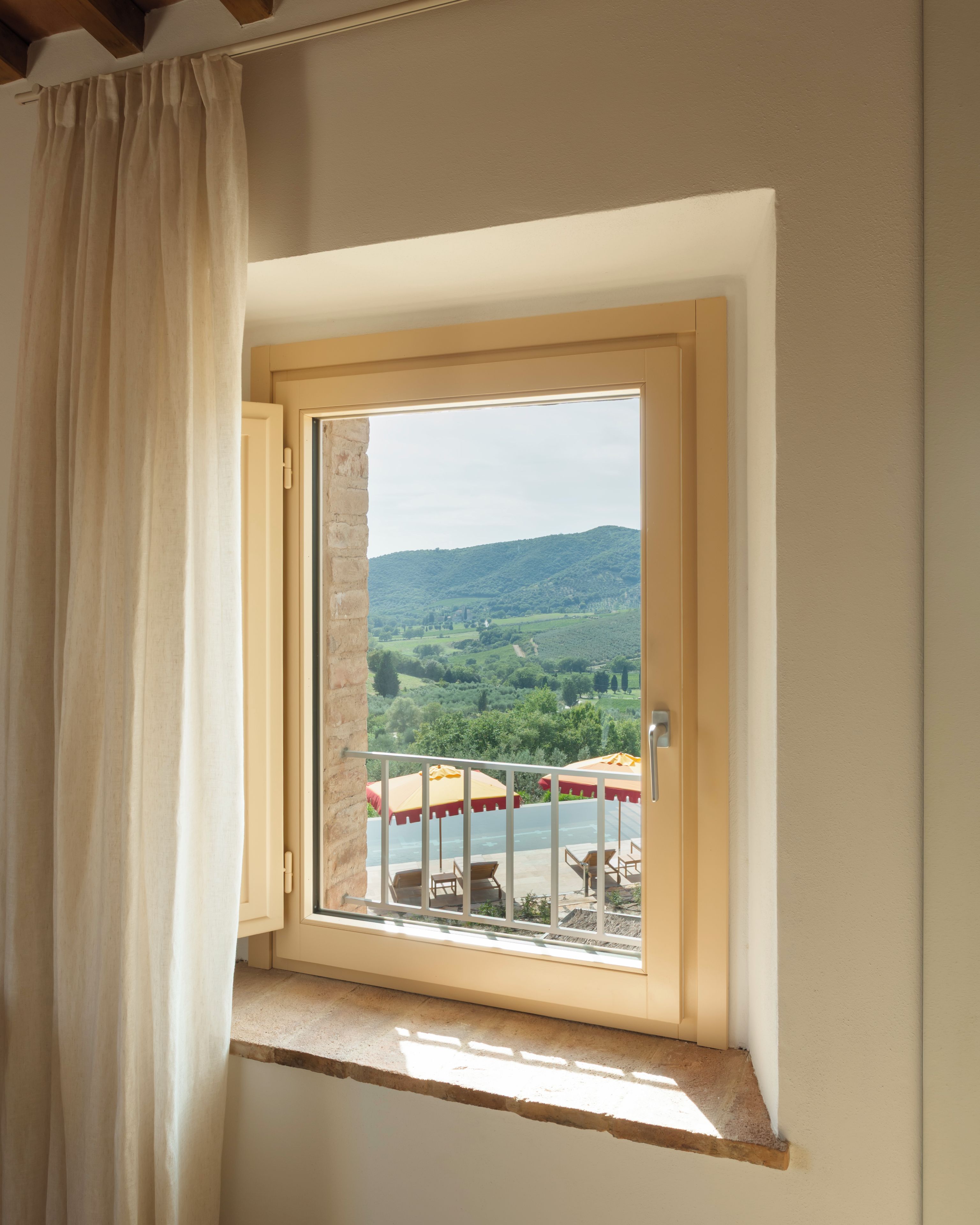 A window with a view of a green landscape and a building with outdoor seating.