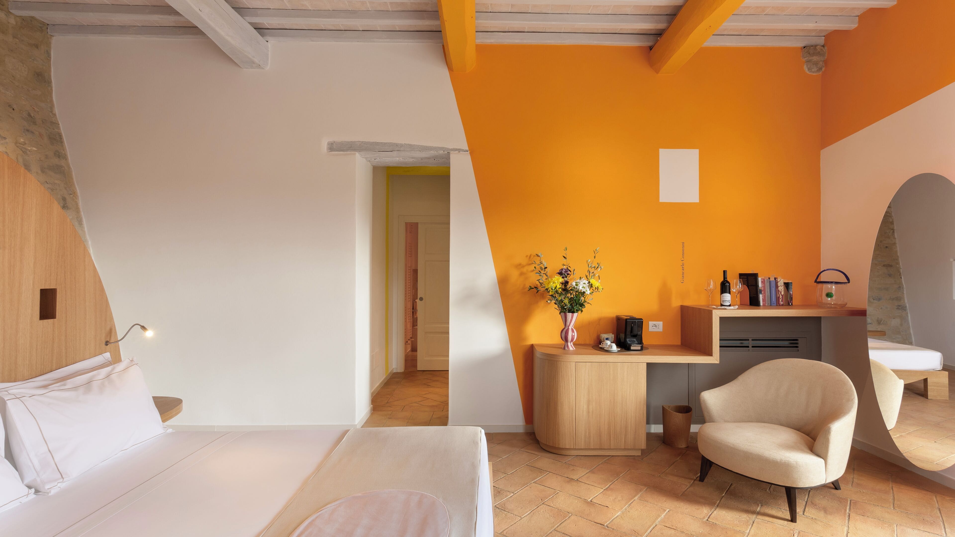 A modern hotel room with a bed, a desk, a chair, and a small table with a vase of flowers.