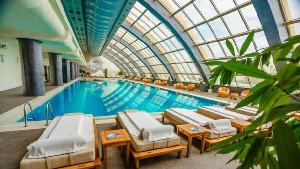 An indoor swimming pool with lounge chairs and a high, arched glass ceiling. - Golden Moon Baku (Baku)