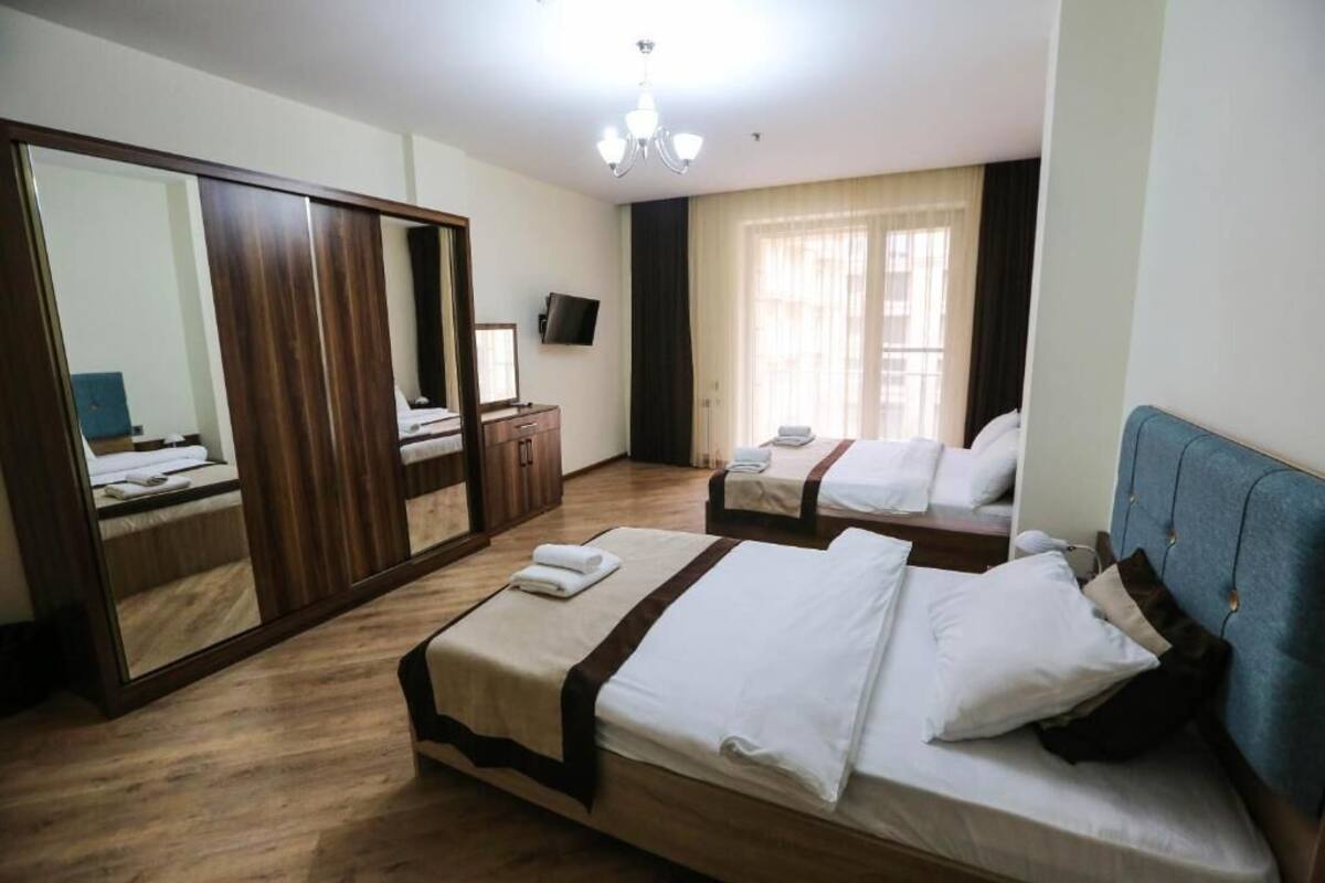 A hotel room with two beds, a large mirror, a wardrobe, a television, and a chandelier.