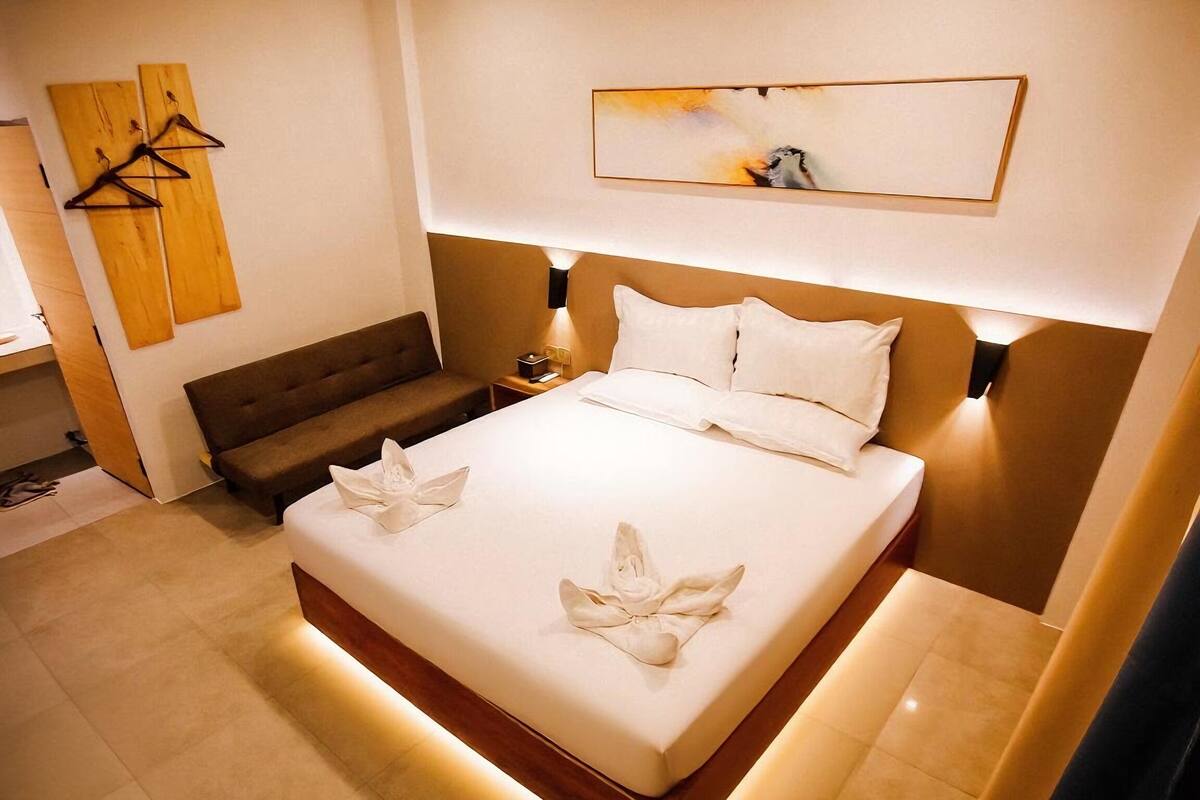Quarto de hotel moderno com uma cama grande, um sofá, uma obra de arte de madeira e uma pintura sobre a cama.