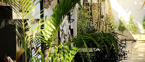 A patio area with a table and chairs, surrounded by various potted plants and a butterfly sculpture.
