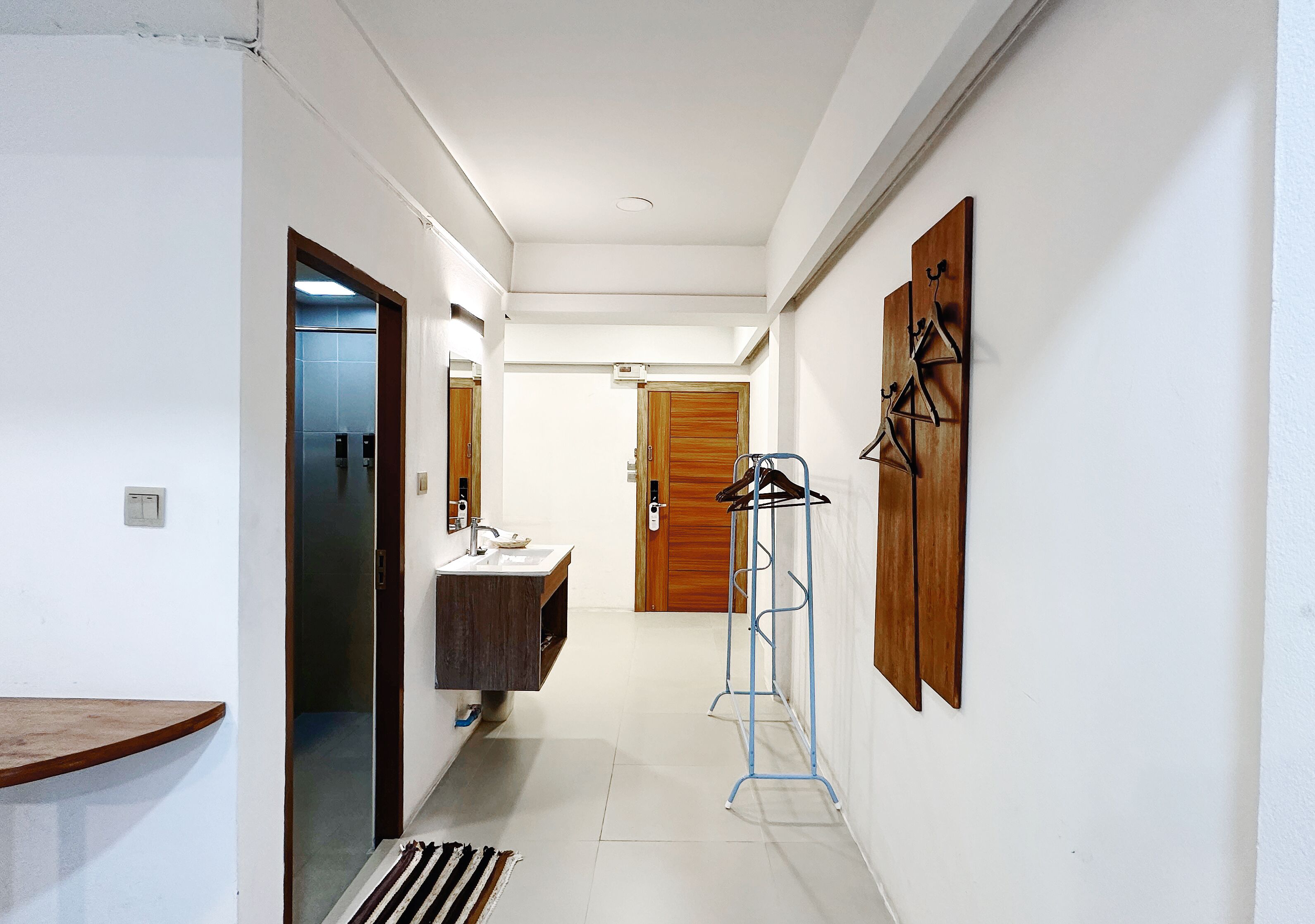 Un couloir étroit avec une porte en bois, un évier et un étendoir métallique.