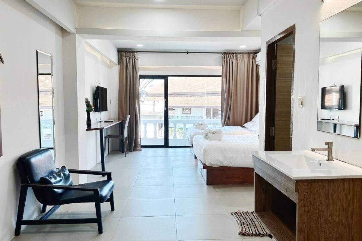Quarto de hotel com cama, escrivaninha, cadeira, espelho grande e banheiro com pia e vaso sanitário.
