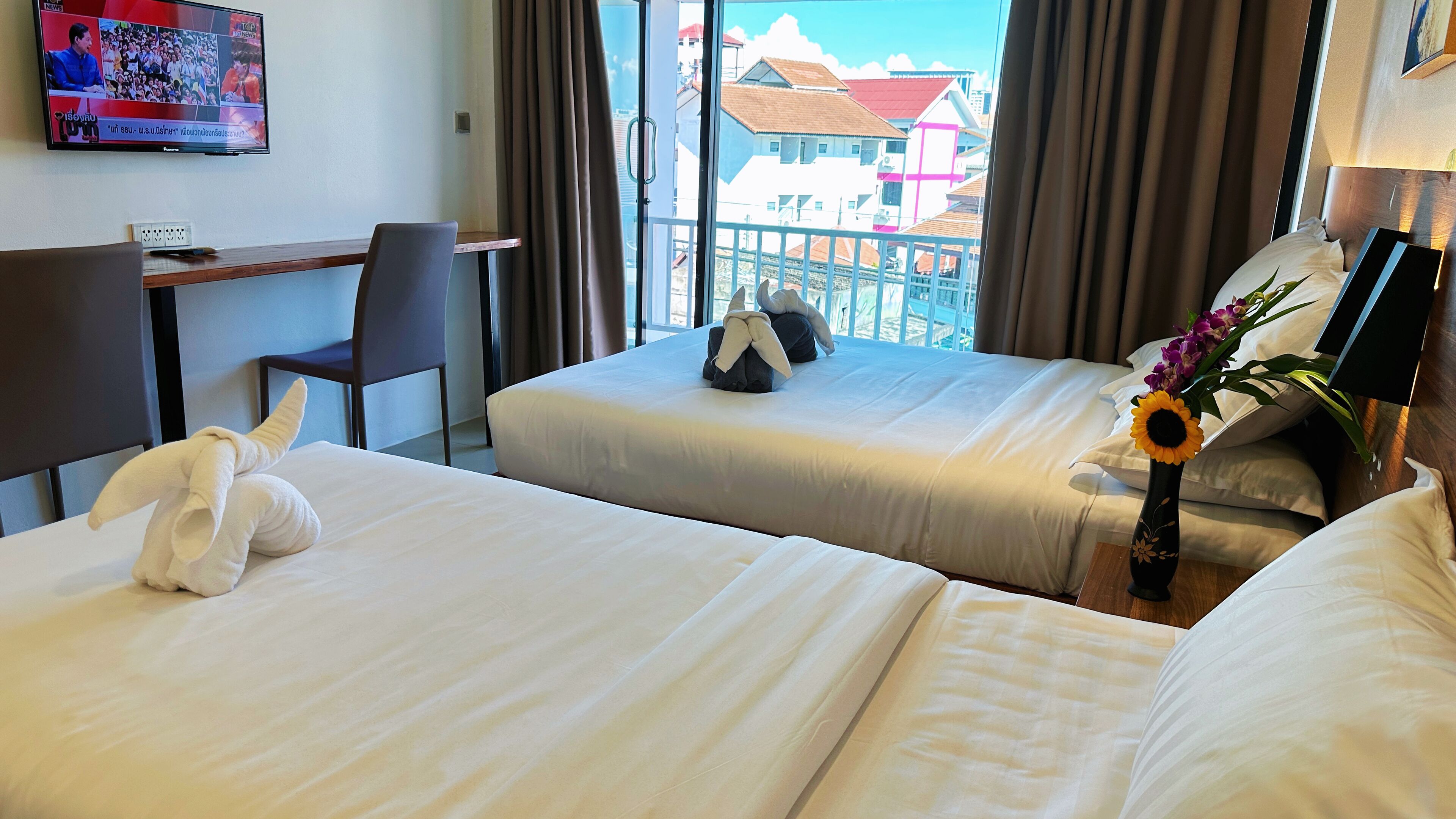 Ein Hotelzimmer mit zwei Betten, einem Schreibtisch, einem Stuhl und einem Fernseher, der einen Nachrichtensender zeigt.