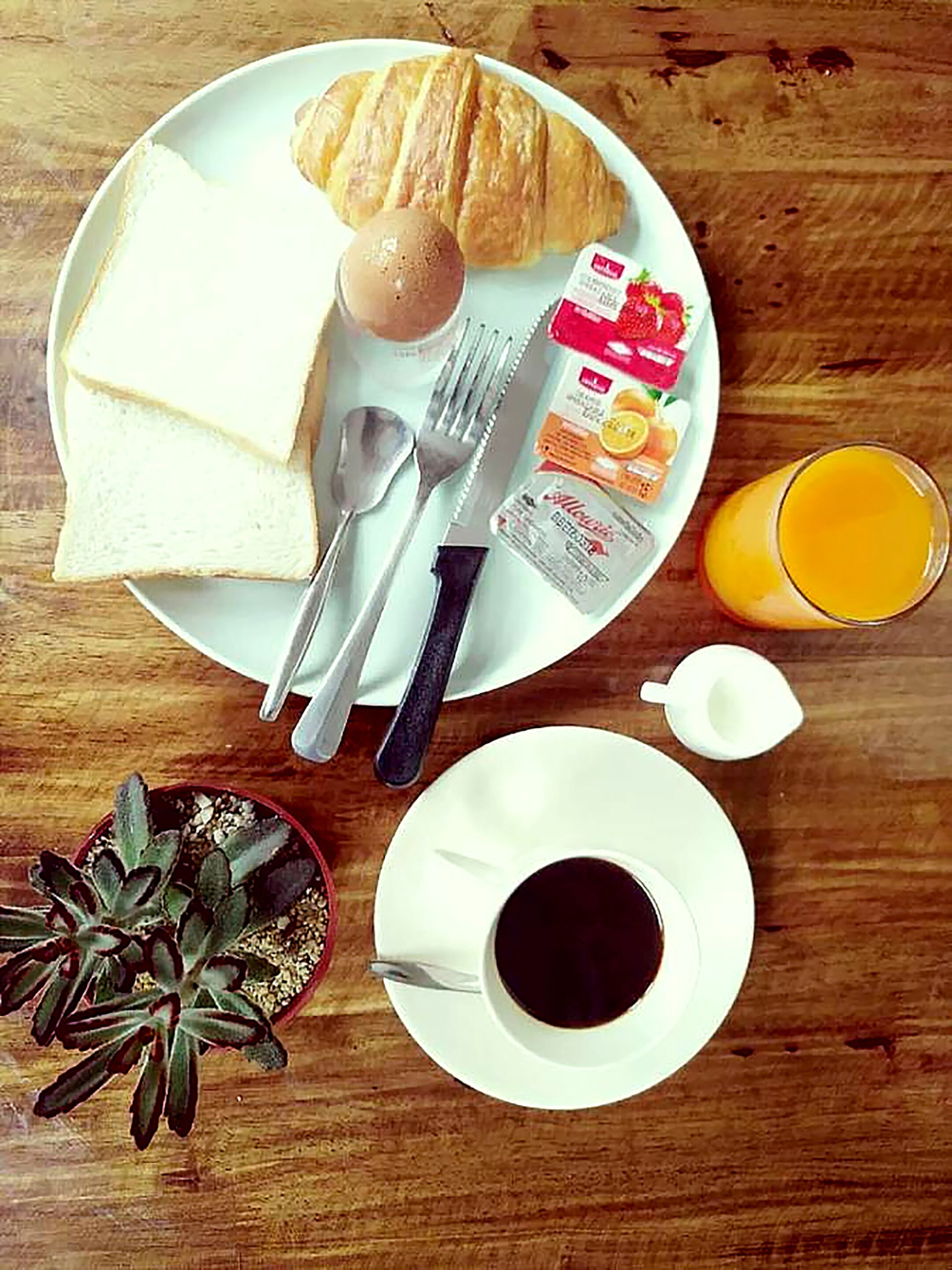 A breakfast plate with croissant, toast, jam, and orange juice on a wooden table.