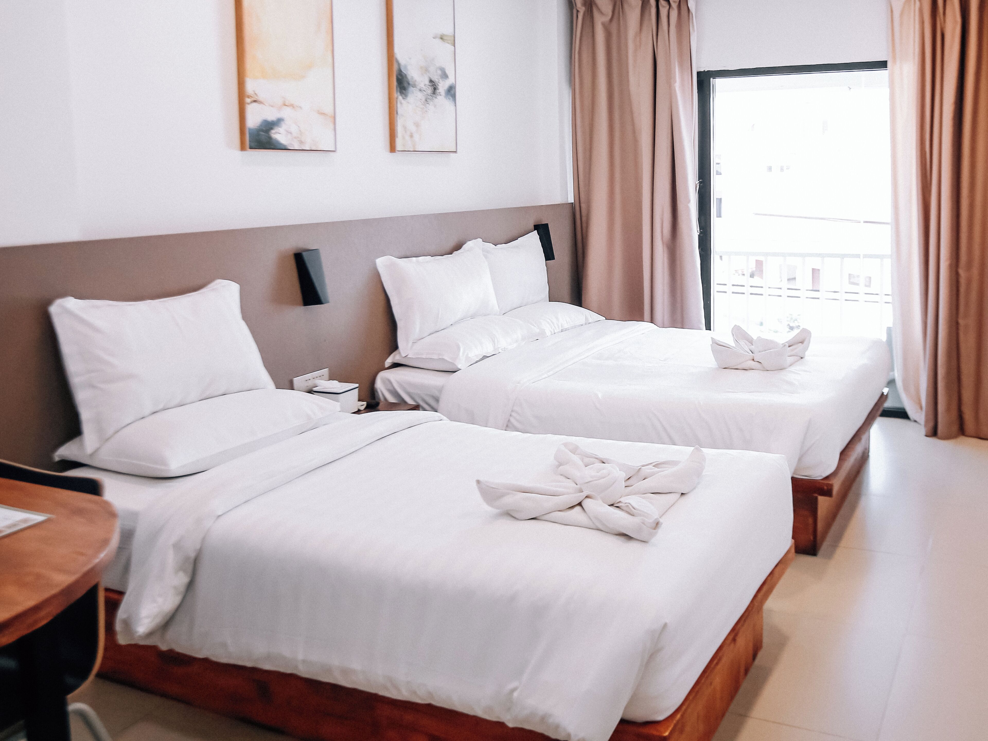 A hotel room with two beds, a wooden headboard, a nightstand, and a window with curtains.