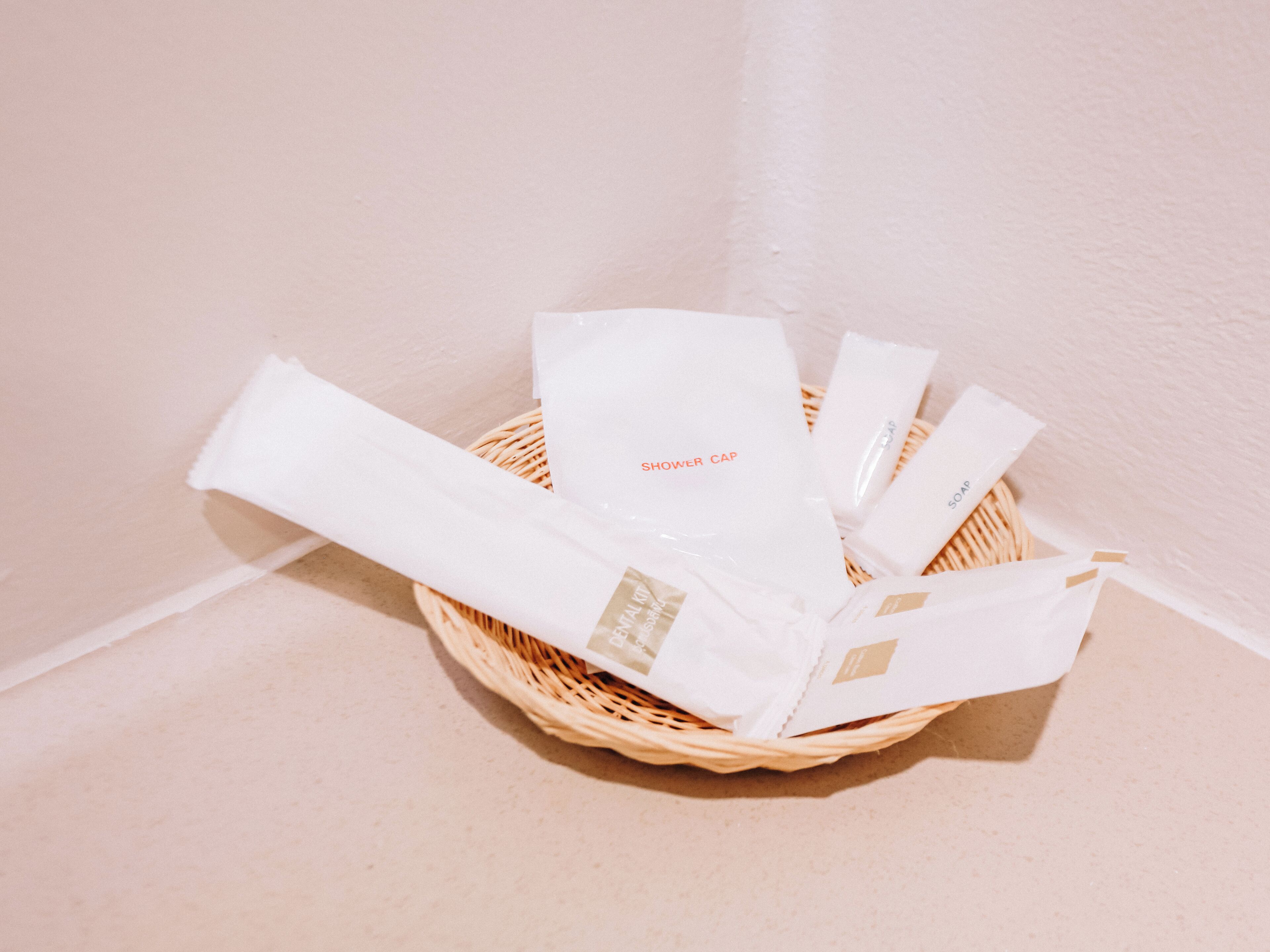 A wicker basket containing various toiletries including a shower cap, soap, and a bar of soap.
