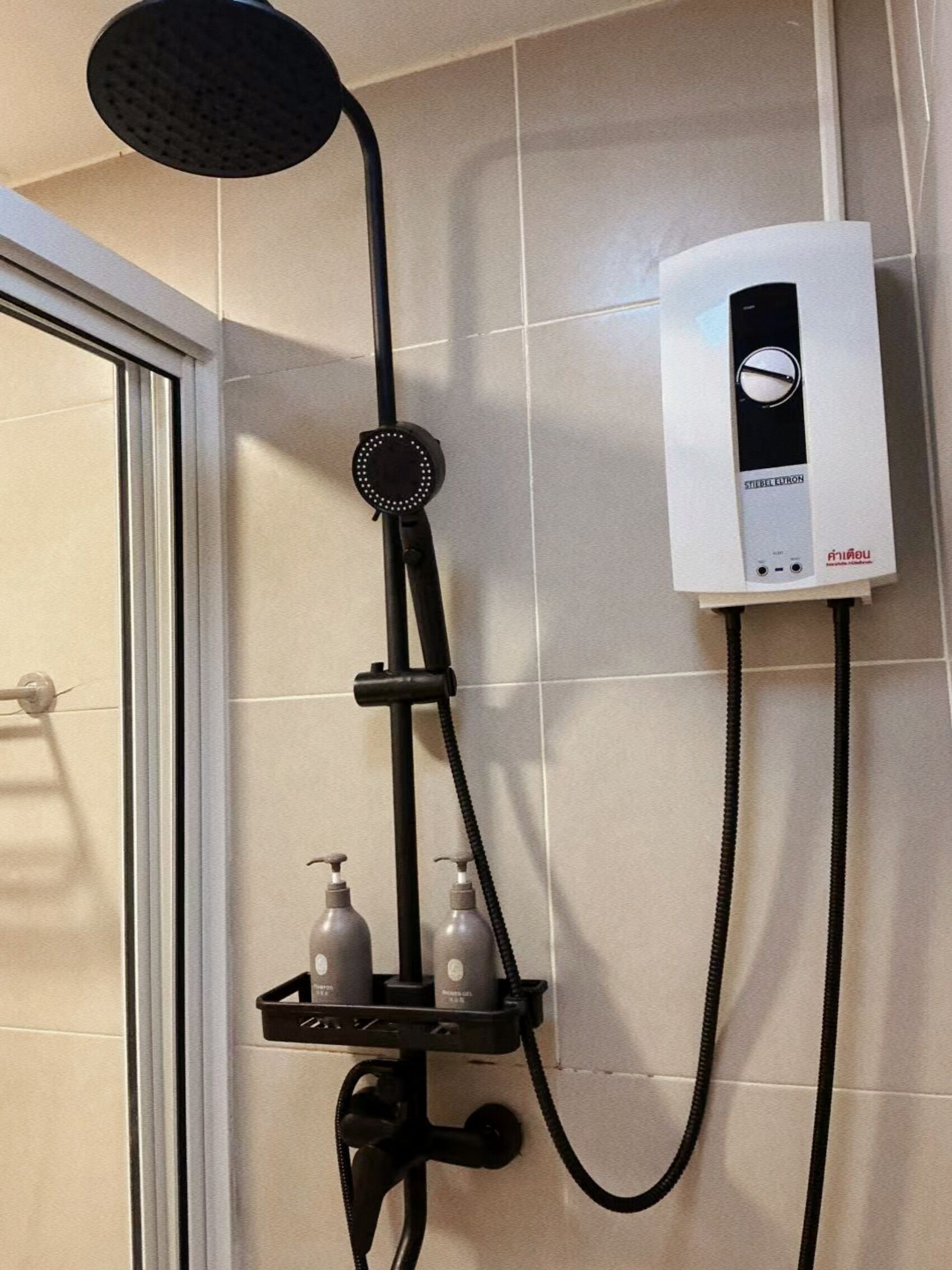 A bathroom with a shower, a wall-mounted heater, and a shelf with toiletries.