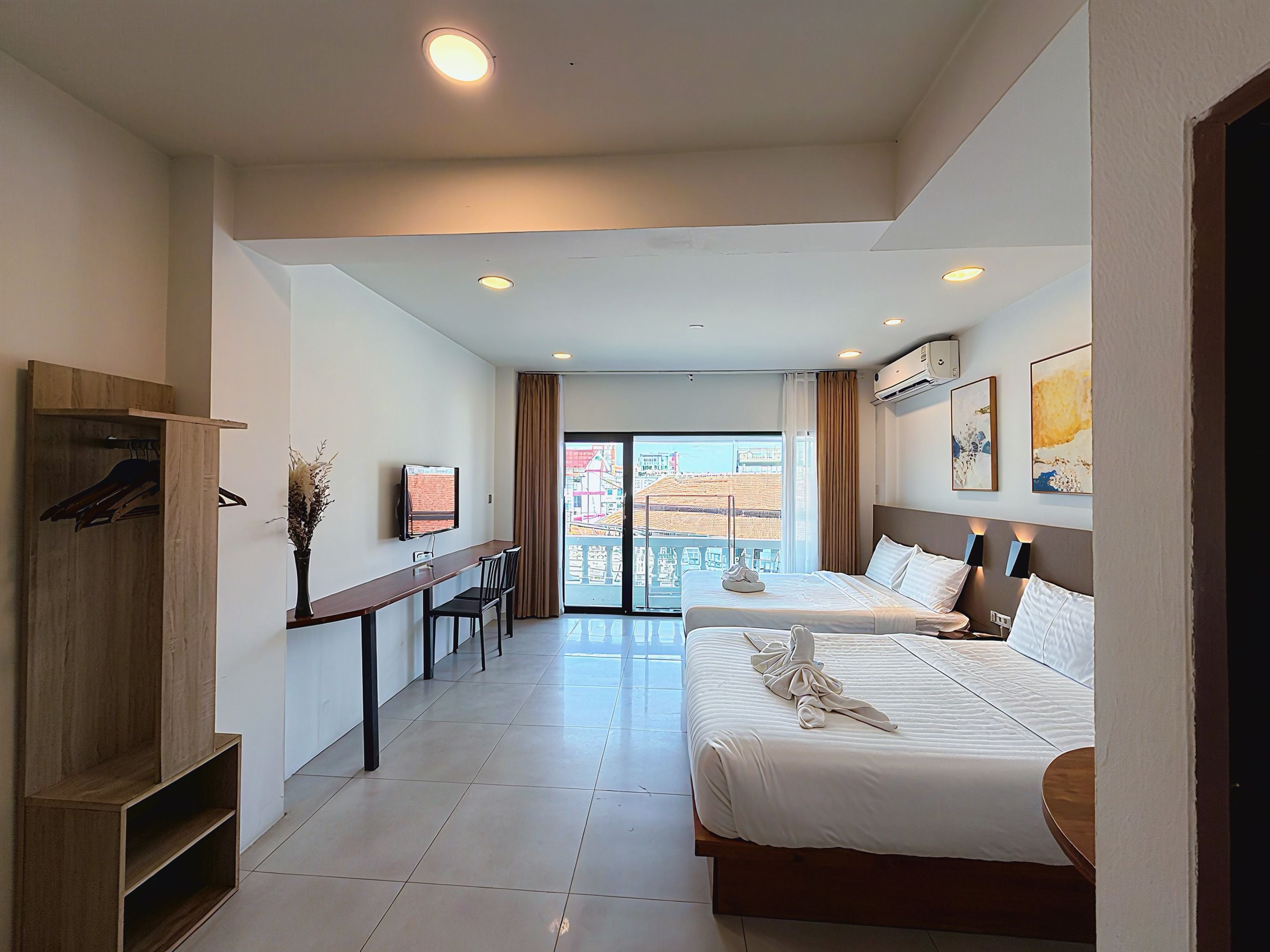 A hotel room with two beds, a desk, a TV, and a view of the city.