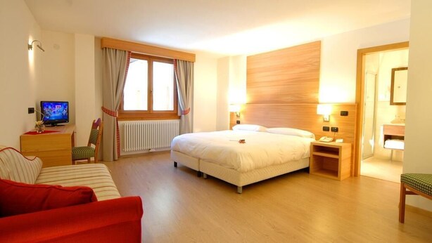 Una habitación de hotel con una cama, un escritorio con ordenador, una silla, un sofá rojo y un cabecero de madera.