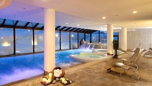 Un área de spa con una amplia piscina interior, una cascada y sillones de descanso.
