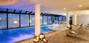 Uma área de spa com uma grande piscina interior, uma cascata e espreguiçadeiras.