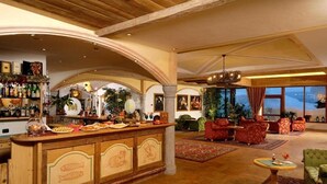 A spacious lobby with a bar area, comfortable seating, and large windows offering a view. - Carlo Magno Hotel Spa Resort (Pinzolo)