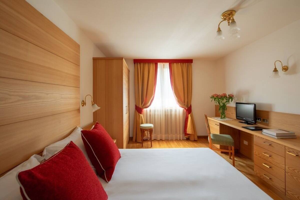 Hotellihuone, jossa on suuri sänky, työpöytä tietokoneella, tuoli ja ikkuna, jossa on verhot.