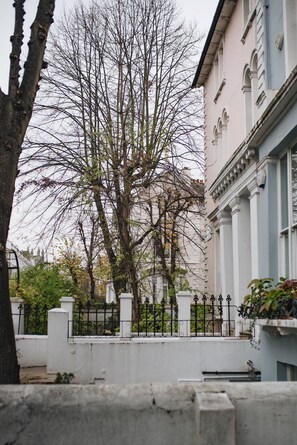 A tree-lined street with a white fence and a building with arched windows. - Glorious 2 Bedroom Apartment (London)
