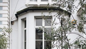 A white building with a black wrought iron balcony, a window, and a small door. - Glorious 2 Bedroom Apartment (London)