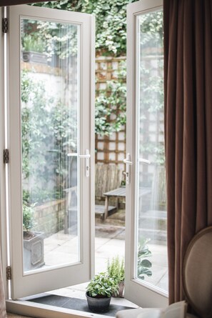 A view through a glass door into a garden with a wooden fence, a bench, and a potted plant. - Glorious 2 Bedroom Apartment (London)