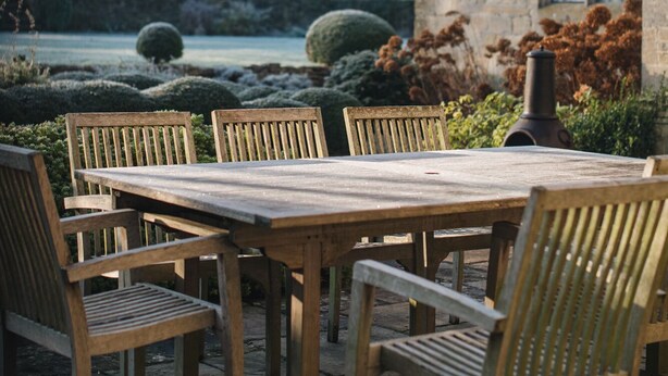 A stone building with a tiled roof, a large wooden table with six chairs, and a well-maintained garden with hedges and a spherical topiary. - Glorious 2 Bedroom Apartment (London)