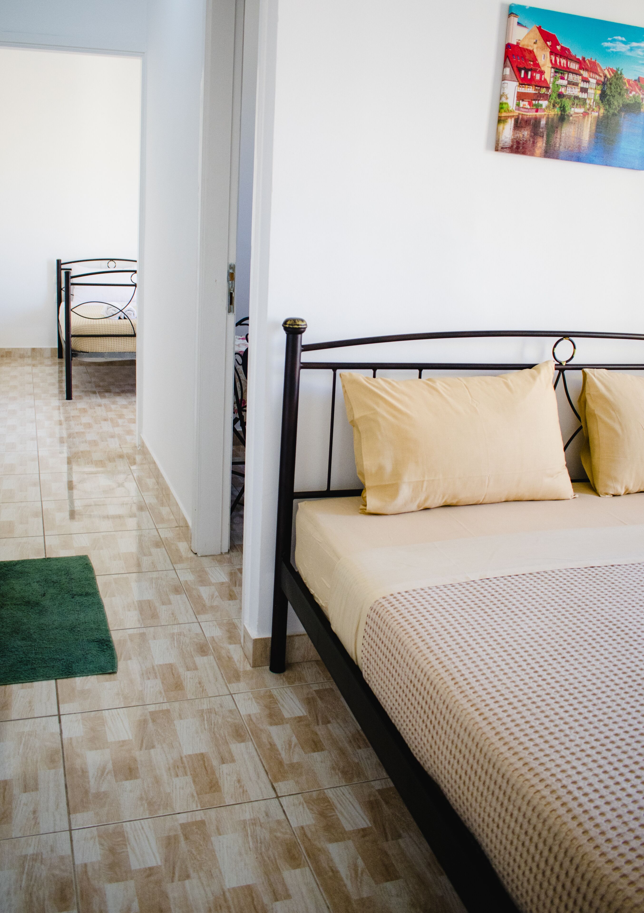 A bedroom with a bed, a green rug, and a painting on the wall.