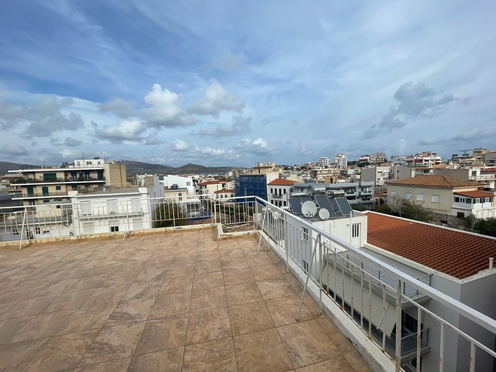 Una terraza en la azotea con vistas a un paisaje urbano, que incluye edificios y una cadena montañosa distante.