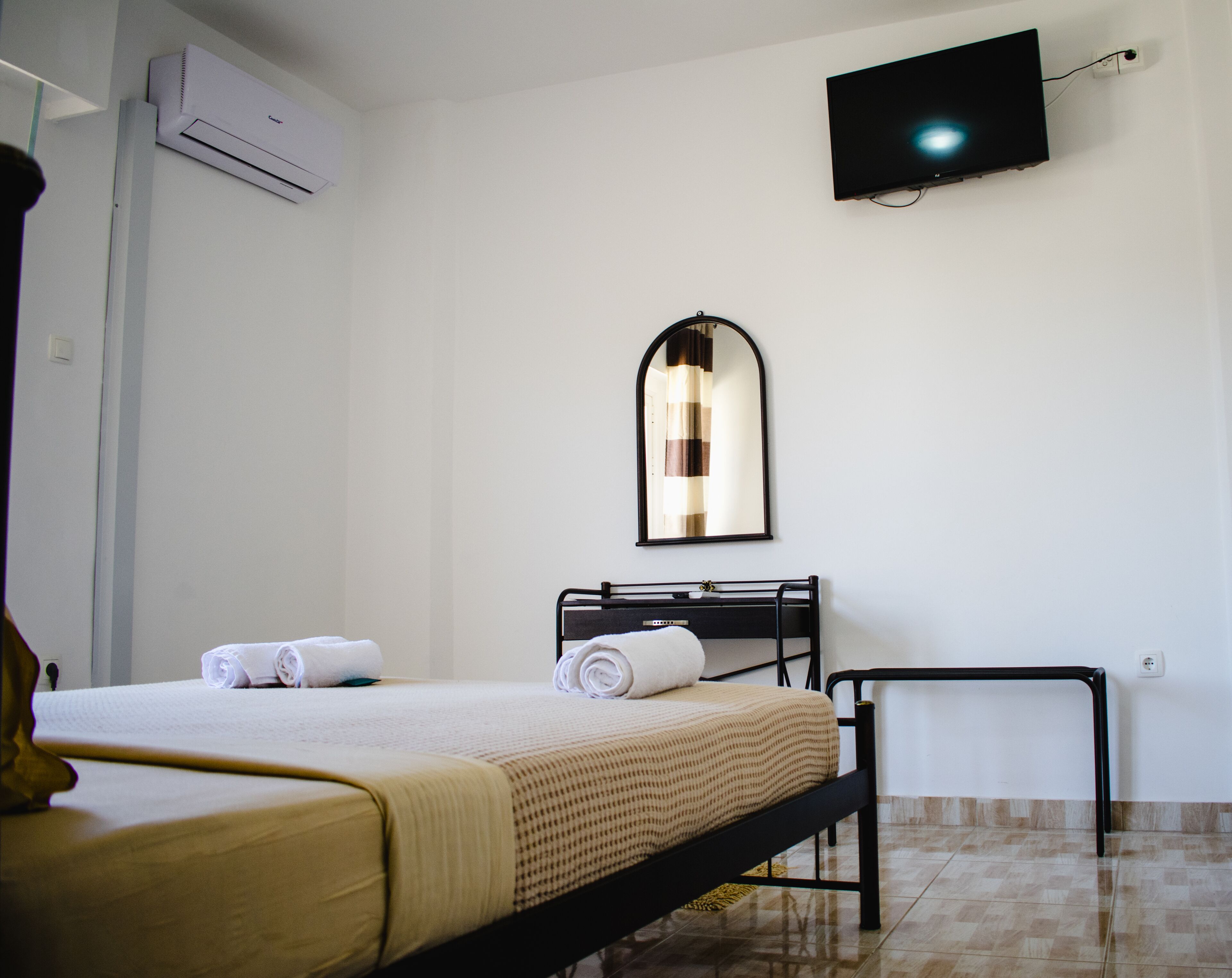 Una habitación de hotel con cama, televisión montada en la pared, espejo y aire acondicionado.
