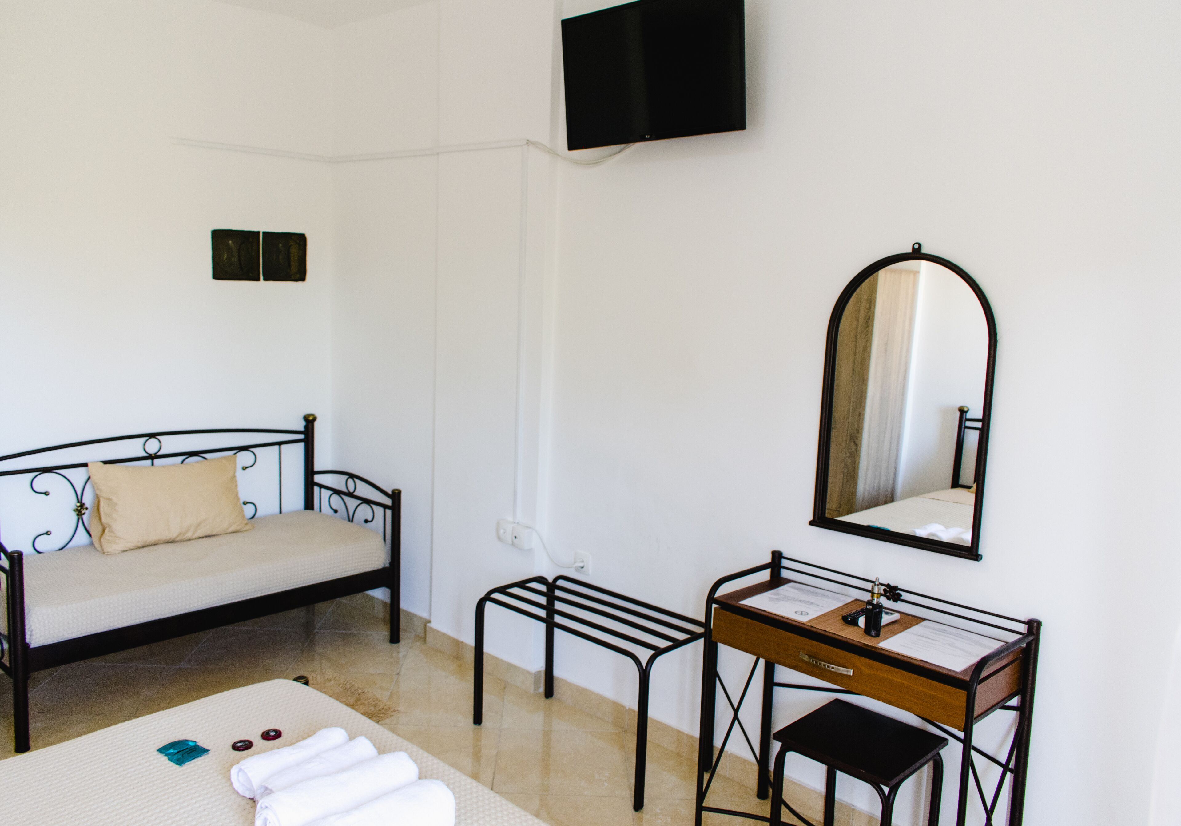Un dormitorio con cama, un escritorio con espejo y televisor montado en la pared.