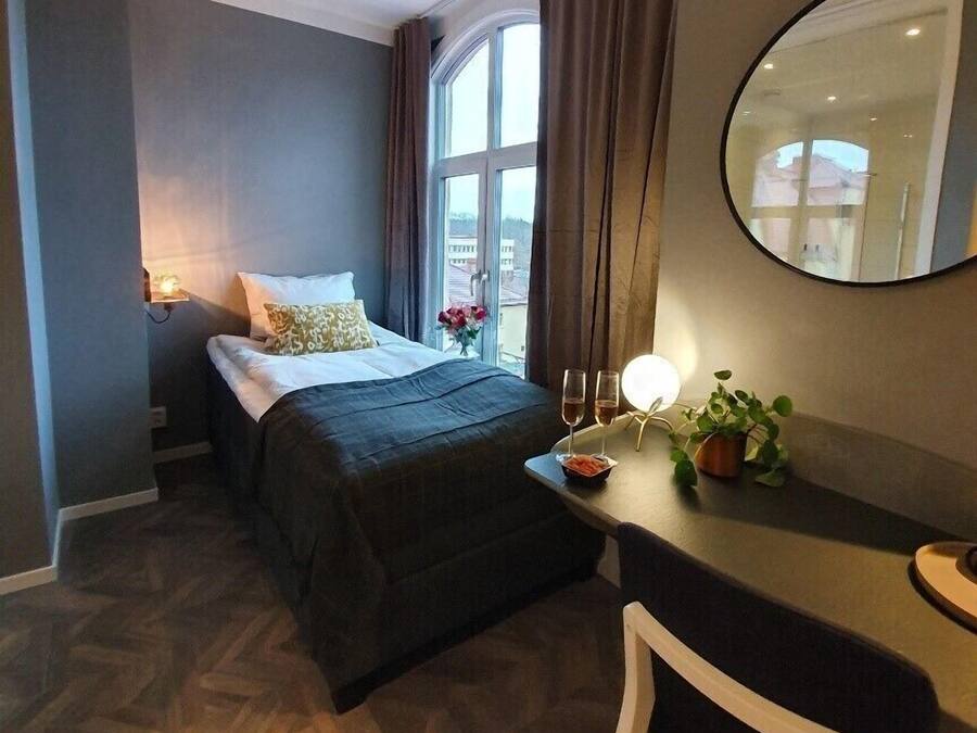 A hotel room with a bed, bedside table, and a desk with a chair.