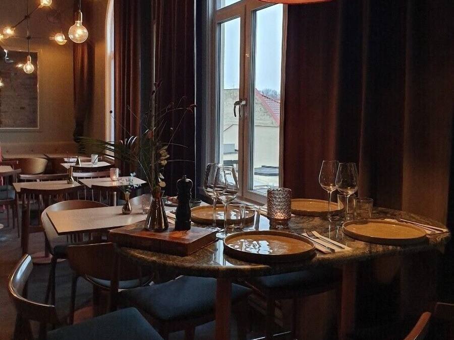 Un restaurante con mesas redondas, sillas y un amplio ventanal con cortinas.