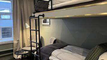 A bunk bed room with a desk and chair, a window with curtains, and a radiator.