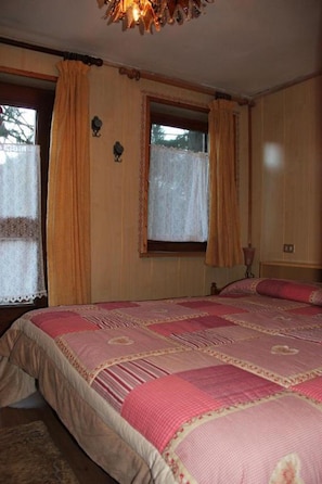 A bedroom with a large bed, wooden walls, and a window with curtains. - Small Box Apartment (primiero san martino di castrozza)
