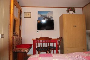 A bedroom with a bed, a wooden wardrobe, a television mounted on the wall, and a chair. - Small Box Apartment (primiero san martino di castrozza)