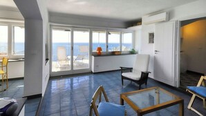 Varanda espaçosa com vista para o mar, área de estar com mesa e porta que dá para outro quarto.