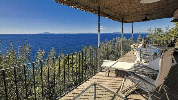 Uma área de estar coberta ao ar livre com vista para o mar, corrimãos de metal e um deck de madeira.