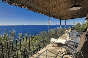 A covered outdoor seating area with a view of the sea, metal railings, and a wooden deck.