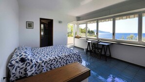 Quarto com cama, escrivaninha e vista para o mar.