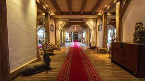 A hallway with a red carpet leading to a room, wooden floors, and a statue on the right. - Chalet Hotel L'Ecrin (Tignes)