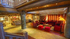 A spacious lobby with a wooden ceiling, stone pillar, red seating, and a bar area. - Chalet Hotel L'Ecrin (Tignes)
