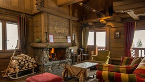 A cozy log cabin interior with a stone fireplace, wooden furniture, and a view of the outdoors. - Chalet Hotel L'Ecrin (Tignes)