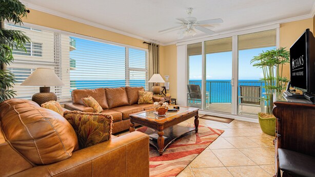 A living room with a leather sofa, a wooden coffee table, and a television. There is a large window with a view of the ocean. - Oceanfront | Heated Pool-Twin Towers #1405 (Daytona Beach Shores)