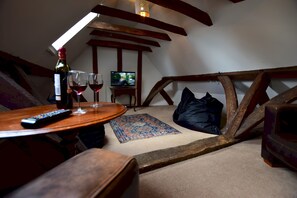 A cozy attic room with a wooden table, two wine glasses, a remote control, a television, and a patterned rug.