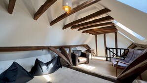 Una camera mansardata con travi a vista in legno, un velux e un divano con una poltrona.