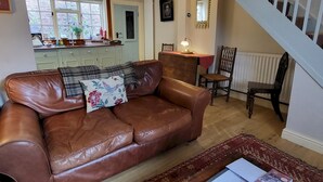 A brown leather sofa with a floral pillow, a dining table with chairs, a staircase, and a kitchen area with cabinets and a window. - 7 Monk Bar Court YORK (York)