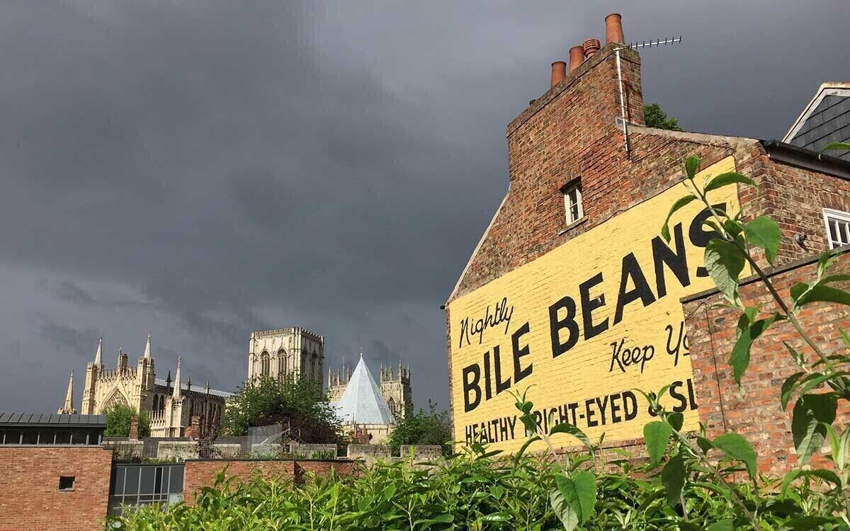 A building with a large sign advertising Bile Beans, a historic building with Gothic architecture, and a cloudy sky.