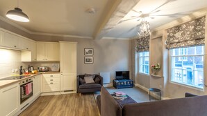 A modern kitchen with white cabinets, a wooden countertop, and a built-in oven. There is a gray sofa and a small table with books. - Apt 3, 71 Micklegate, YORK (York)