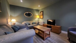 A living room with a sofa, a coffee table, a TV stand, and a lamp. - Trinity Cottage, YORK (York)