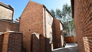 A brick building with a small window and a door, surrounded by a paved courtyard. - Trinity Cottage, YORK (York)